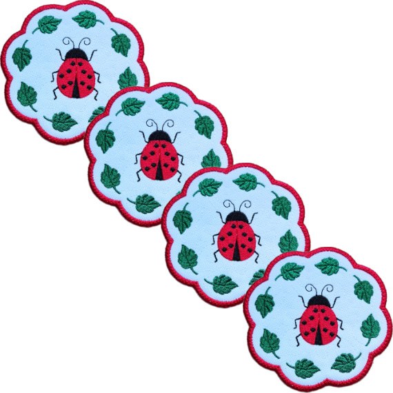 Set of four embroidered ladybird candle coasters with bright stitched ladybirds, green leaf details and red scalloped edging.