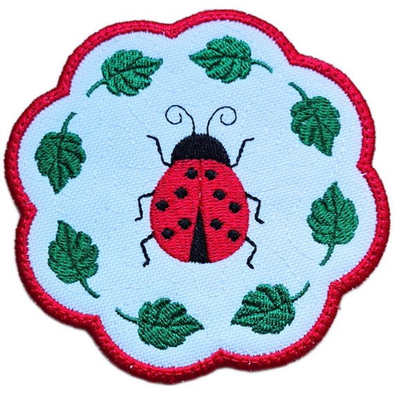 Close up of an embroidered ladybird candle coaster with a bright stitched ladybird, green leaf details and red scalloped edging.