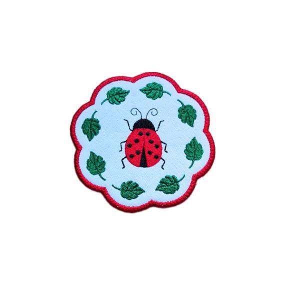 Embroidered ladybird candle coaster with a bright stitched ladybird in the centre, green leaf details and scalloped edging.