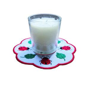 Embroidered ladybird candle mat with bright stitched ladybirds, leafy details, scalloped edging and a glass jar candle displayed in the centre.