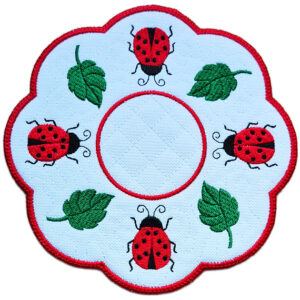 Close up of an embroidered ladybird candle mat showing bright stitched ladybirds, green leaf details, scalloped edging and a central circle for a candle or display item.