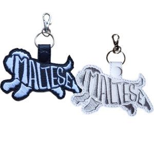 Embroidered Maltese word art keyrings in black and white faux leather, shown with metal split rings and lobster clasps.