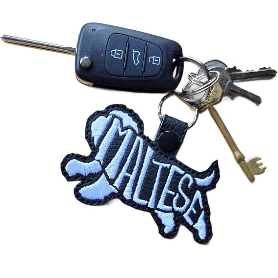 Black embroidered Maltese word art keyring attached to a set of keys, showing how it looks in everyday use.
