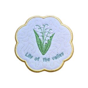 Embroidered May birth flower candle coaster with Lily of the Valley flowers, green leaves, stitched text and a softly scalloped border.