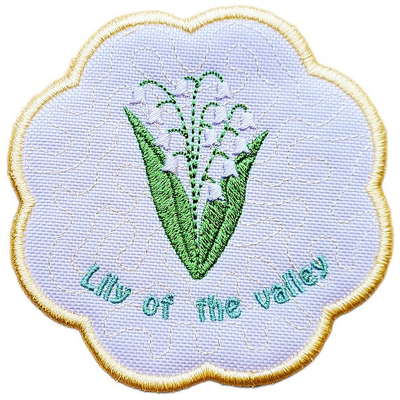 Close up of an embroidered May birth flower candle coaster with Lily of the Valley flowers, green leaves, stitched text and a scalloped border.