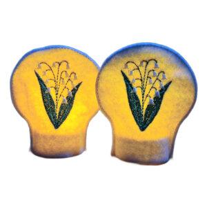 Lit embroidered May birth flower tealight covers on white felt, glowing warmly with Lily of the Valley flowers over battery operated LED tealights.