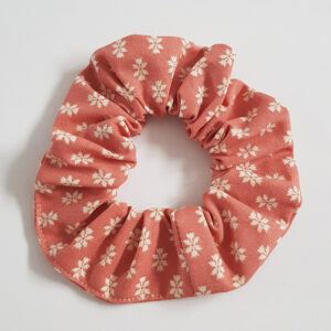 Orange cotton scrunchie with tiny white floral sprigs on a white background.