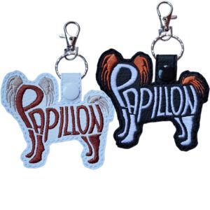 Embroidered Papillon word art keyrings in black and white faux leather, shown with metal split rings and lobster clasps.