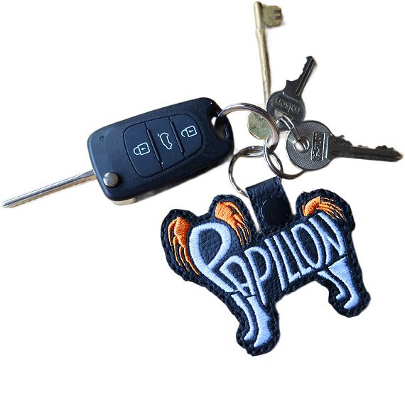 Black embroidered Papillon word art keyring attached to a set of keys, showing how it looks in everyday use.