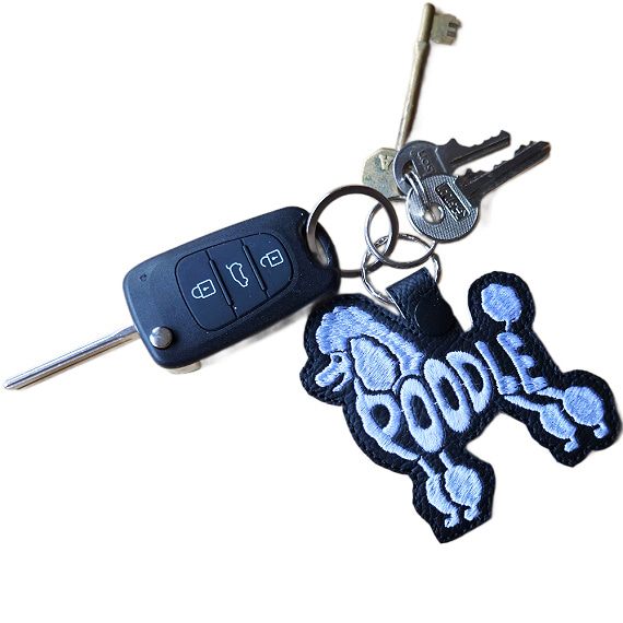 Black embroidered Poodle word art keyring attached to a set of keys, showing how it looks in everyday use.