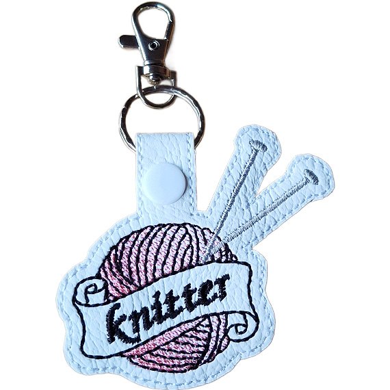 White faux leather knitting keyring embroidered with a pink yarn ball, silver knitting needles and banner reading 'Knitter', finished with a metal clasp.