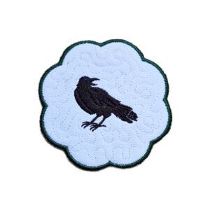 Embroidered raven candle coaster with a striking black raven design, scalloped edging and gothic inspired decorative styling.