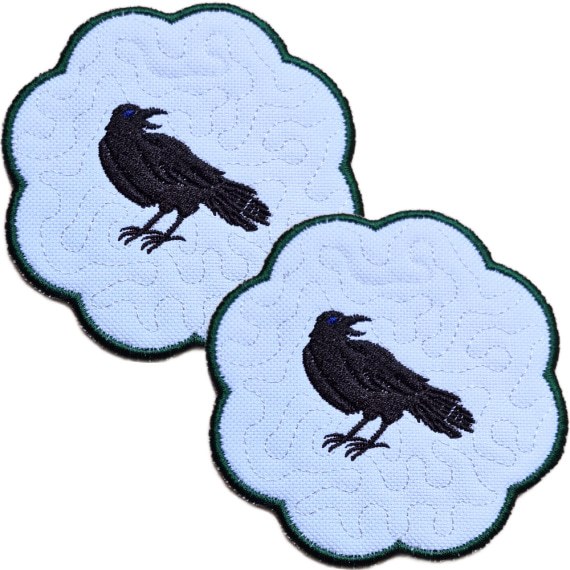 Set of two embroidered raven candle coasters with striking black raven designs, scalloped edging and subtle gothic background detail.