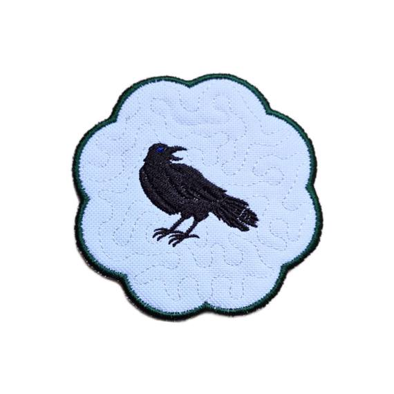 Embroidered raven candle coaster with a striking black raven design, scalloped edging and gothic inspired decorative styling.