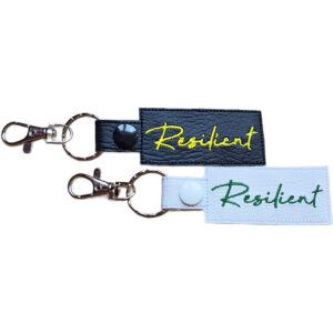 Embroidered Resilient keyring in faux leather, with the word 'Resilient' stitched on black and white backgrounds with sturdy metal hardware.