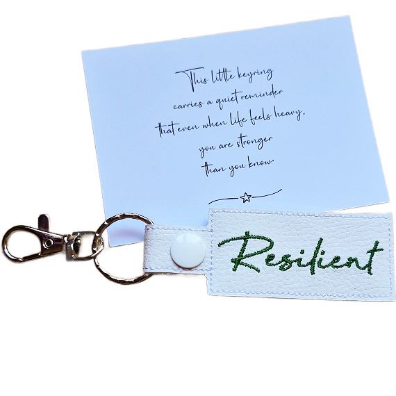Embroidered Resilient keyring in white faux leather, shown beside a matching keepsake card with an encouraging message about strength.
