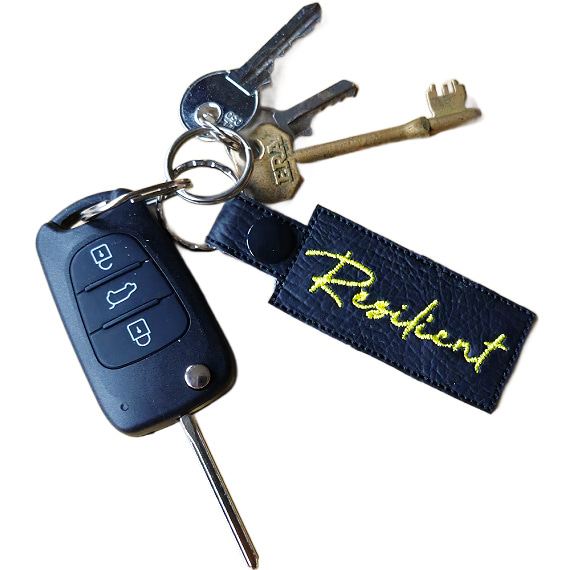 Embroidered Resilient keyring attached to a set of keys, featuring black faux leather and the word 'Resilient' stitched in yellow.