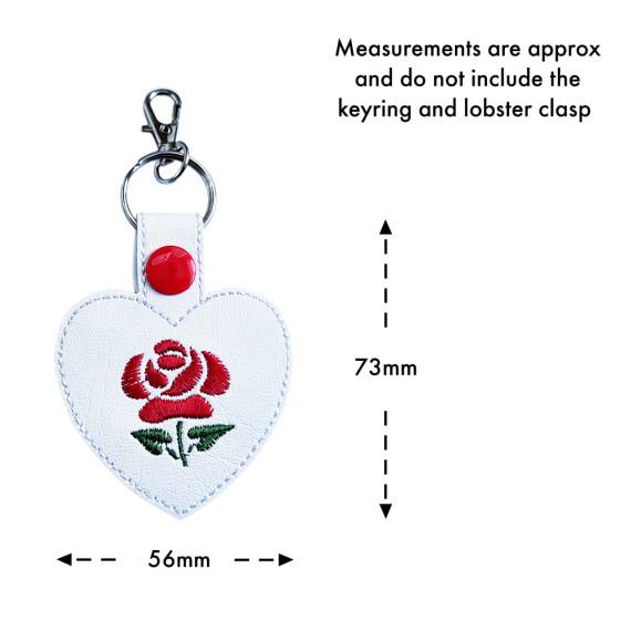 White faux leather rose heart keyring with red embroidered rose, shown with measurement arrows indicating an approximate size of 73mm x 56mm, excluding the keyring and clasp.