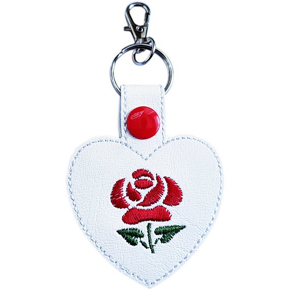 White faux leather heart keyring with a red embroidered rose design, red snap fastening and silver lobster clasp hardware.