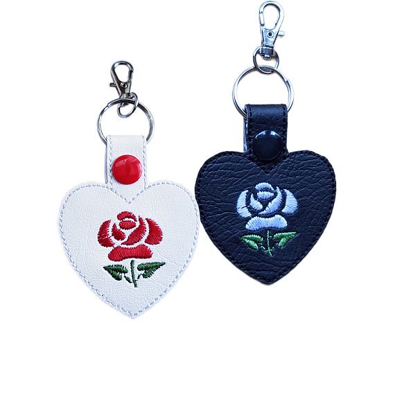 Embroidered rose heart keyrings in black and white faux leather, each with a stitched rose design, snap fastening and silver key clip.