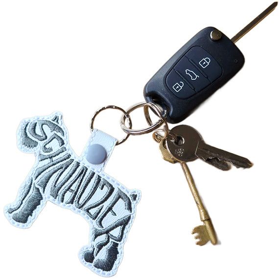 White embroidered Schnauzer word art keyring attached to a set of keys, showing how it looks in everyday use.