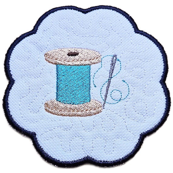 Close up of an embroidered sewing candle coaster with a stitched thread spool, needle and thread detail, scalloped edging and soft craft room style background.