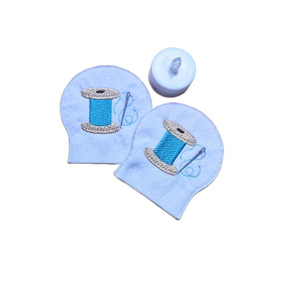 Set of two embroidered sewing tealight covers made from soft felt, shown with an LED tealight and stitched thread spool designs for a cosy craft room display.