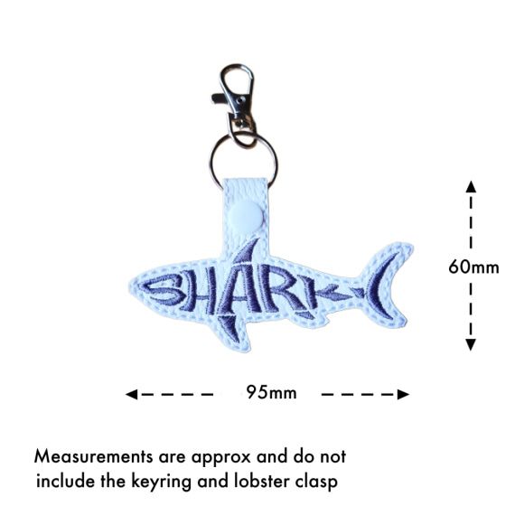 White faux leather shark word art keyring with grey embroidered 'Shark' lettering, shown with measurement arrows indicating an approximate size of 60mm x 95mm, excluding the keyring and lobster clasp.
