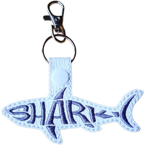 White faux leather shark word art keyring with grey embroidered 'Shark' lettering, white snap fastening and silver lobster clasp hardware.