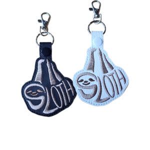 Black and white faux leather sloth word art keyrings with embroidered 'Sloth' lettering, snap fastenings and silver lobster clasp hardware.