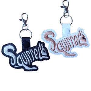 Black and white faux leather squirrel word art keyrings with embroidered 'Squirrel' lettering, snap fastenings and silver lobster clasp hardware.
