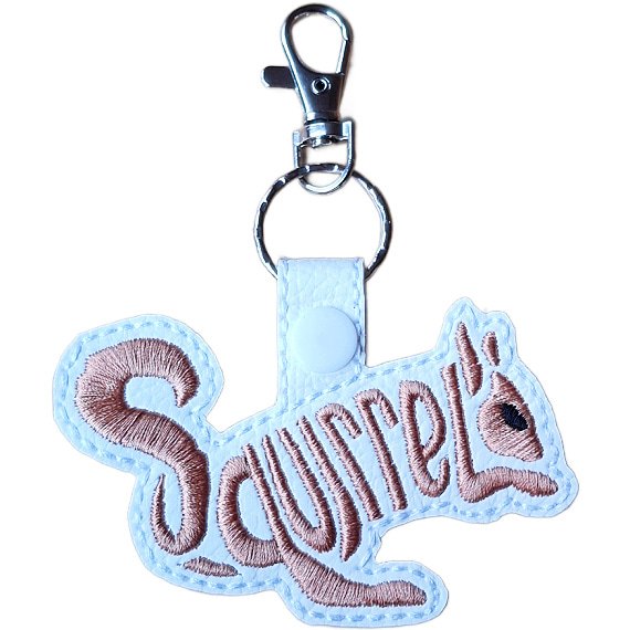 White faux leather squirrel word art keyring with brown embroidered 'Squirrel' lettering, white snap fastening and silver lobster clasp hardware.