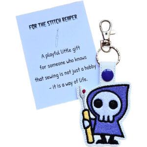White faux leather Stitch Reaper keyring with a purple cloak and yellow seam ripper, shown with a keepsake card reading 'For the Stitch Reaper'.