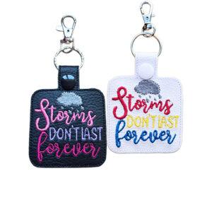 Black and white faux leather Storms Don't Last Forever keyrings with colourful embroidered wording, raincloud design, snap fastenings and silver lobster clasp hardware.