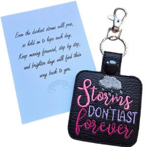 Black faux leather Storms Don't Last Forever keyring with colourful embroidered wording and raincloud design, shown beside a white keepsake card with hopeful reminder wording.