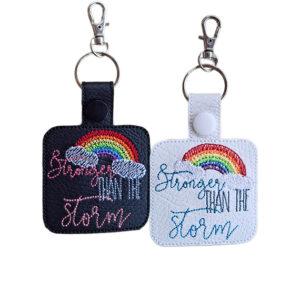 Black and white faux leather Stronger Than the Storm keyrings with embroidered rainbow, cloud design, uplifting wording, snap fastenings and silver lobster clasp hardware.