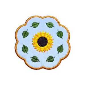 Embroidered sunflower candle coaster with a bright yellow sunflower in the centre, green leaves around the edge and a golden scalloped border.