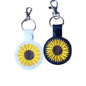 Black and white faux leather sunflower keyrings with bright embroidered sunflower designs, snap fastenings and silver lobster clasp hardware.