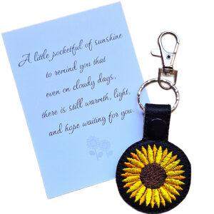 Black faux leather sunflower keyring with bright yellow embroidered flower design, shown beside a white keepsake card with sunshine-themed wording.