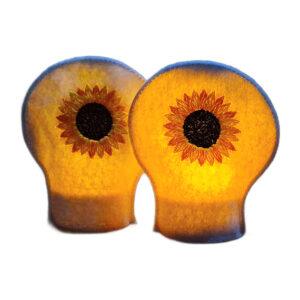 Two lit sunflower tealight covers glowing warmly over LED tealights, with embroidered sunflower designs on white felt.