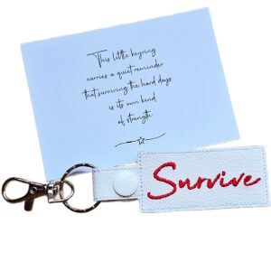 Embroidered Survive keyring in white faux leather, shown beside a matching keepsake card with an encouraging message about surviving hard days.