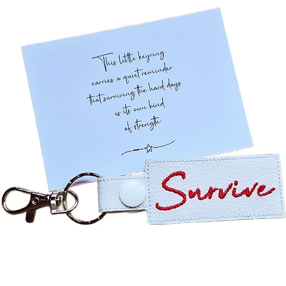 Embroidered Survive keyring in white faux leather, shown beside a matching keepsake card with an encouraging message about surviving hard days.