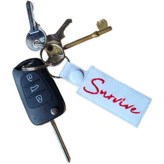 Embroidered Survive keyring attached to a set of keys, featuring white faux leather and the word 'Survive' stitched in red.