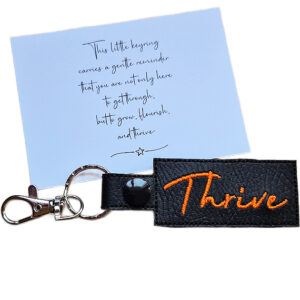 Embroidered Thrive keyring in black faux leather, shown beside a matching keepsake card with an uplifting message about growing, flourishing and thriving.