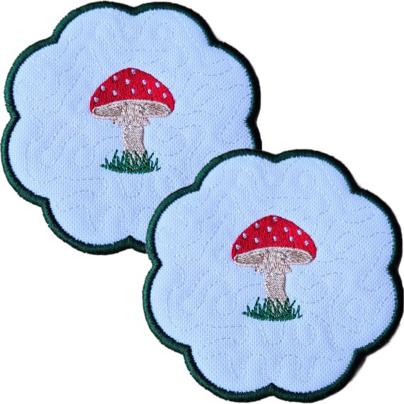 Set of two embroidered toadstool candle coasters with red stitched toadstools, grassy details, scalloped edging and matching woodland style.