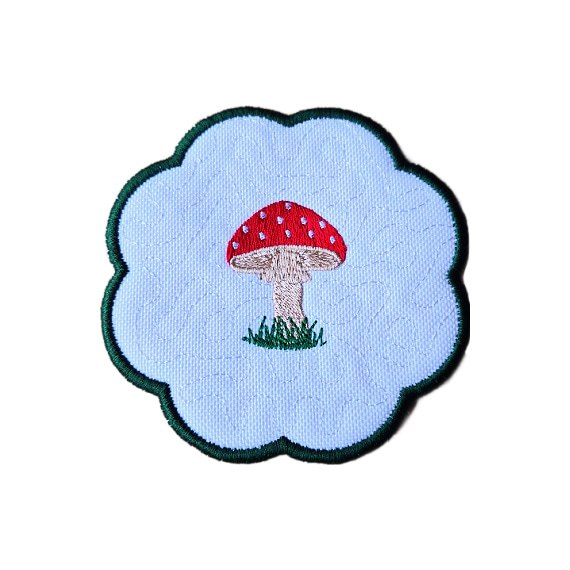 Embroidered toadstool candle coaster with a red stitched toadstool, grassy detail and scalloped edging.