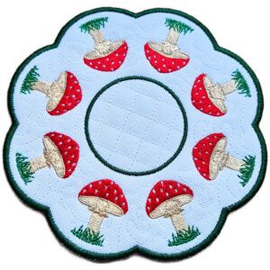 Close up of an embroidered toadstool candle mat showing red stitched toadstools, grassy details, scalloped edging and a central circle for a candle or display item.