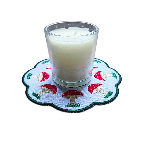 Embroidered toadstool candle mat with red stitched toadstools, grassy details, scalloped edging and a glass jar candle displayed in the centre.