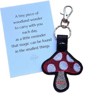 Embroidered toadstool mushroom keyring in black faux leather displayed beside a keepsake card with woodland wonder wording.