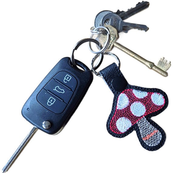 Black faux leather toadstool mushroom keyring attached to a set of keys, showing its size and use as an everyday key charm.
